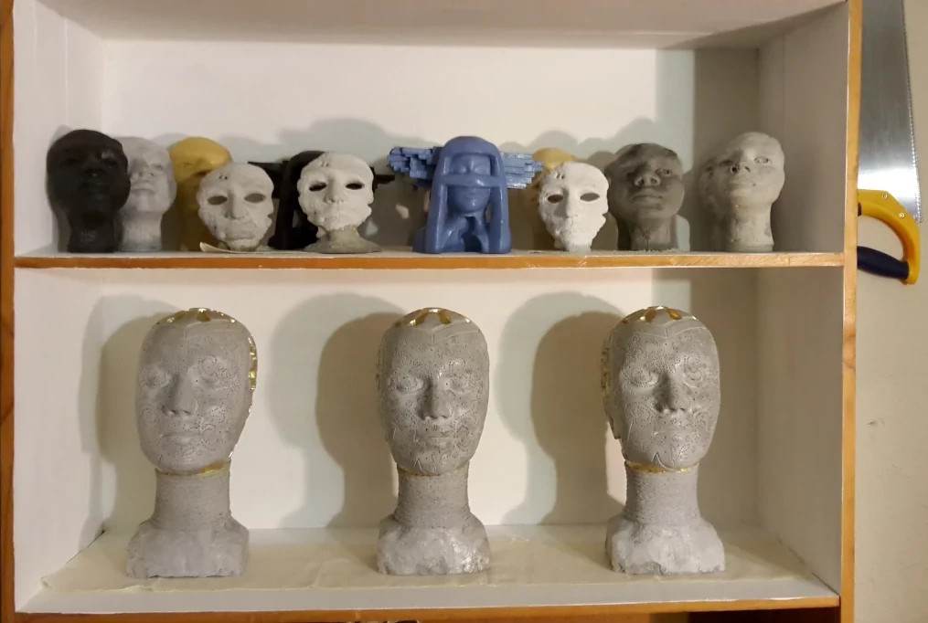 Three sculptural heads with other sculptures on a shelf in the studio.