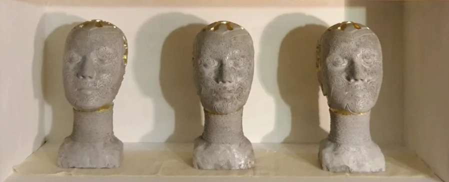 Three sculptural heads with other sculptures on a shelf in the studio.
